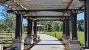 A covered walkway with a gravel path, benches, and a view of a park.