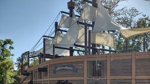A pirate-themed play structure with a ship's wheel, a slide, and a climbing net.