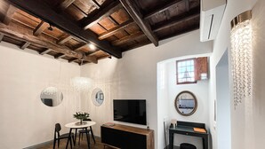 Een woonkamer met een houten plafond, een televisie, een ronde spiegel en een kleine tafel met stoelen.