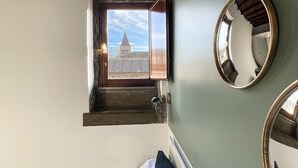Een kamer met een bed, een raam met uitzicht op een gebouw en een ronde spiegel aan de muur.