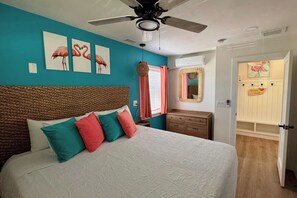 A bedroom with a bed, a ceiling fan, a dresser, and a door leading to another room.