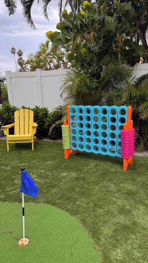A backyard with artificial grass, a blue flag, a yellow chair, and a blue and orange play structure.