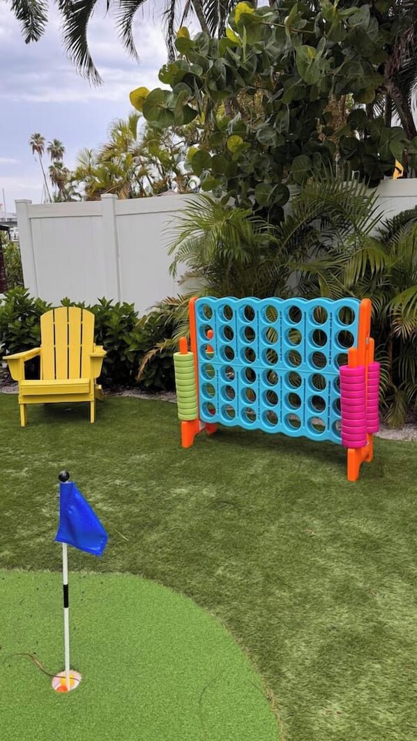 Un patio con césped artificial, una bandera azul, un sillón amarillo y un módulo de juegos azul y naranja.