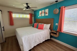 A bedroom with a bed, a ceiling fan, a window with blinds, and a wall with artwork. - The Flamingo Waterfront Bungalow (Madeira Beach)