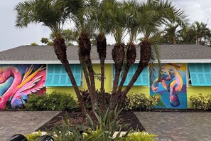 A building with vibrant murals of a flamingo and a parrot, surrounded by palm trees and a brick pathway.