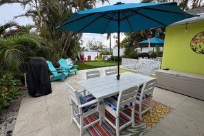 A patio area with a table and chairs, a blue umbrella, and a grill. - The Flamingo Waterfront Bungalow (Madeira Beach)