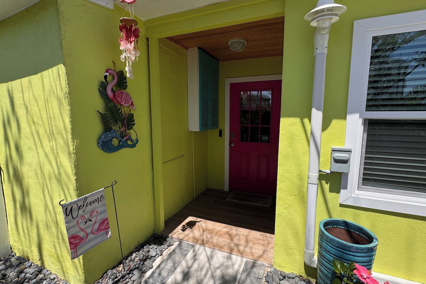 A house with a bright yellow exterior, a pink door, and a welcome sign with flamingos.