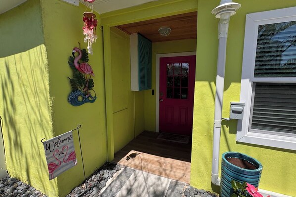 A house with a bright yellow exterior, a pink door, and a welcome sign with flamingos. - The Flamingo Waterfront Bungalow (Madeira Beach)