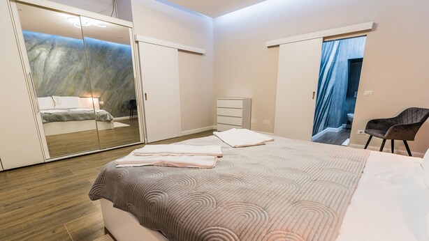 A modern bedroom with a large bed, a wardrobe, a dresser, and a chair.