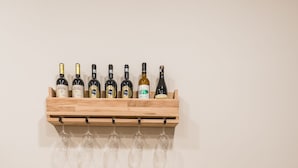 A wooden table with two grey barstools, a shelf with wine bottles and glasses, and a yellow vase.