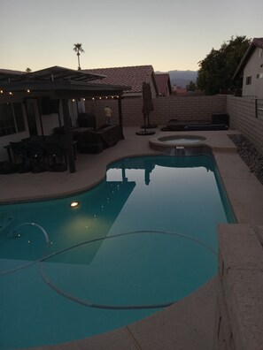 A swimming pool with a hot tub, outdoor furniture, and string lights.