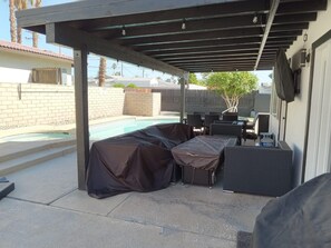 A covered patio area with a pool, outdoor furniture, and a barbecue grill.