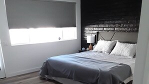 A bedroom with a bed, a nightstand, a lamp, and a window with blinds. - Located in the heart of Palm Desert (Palm Desert)