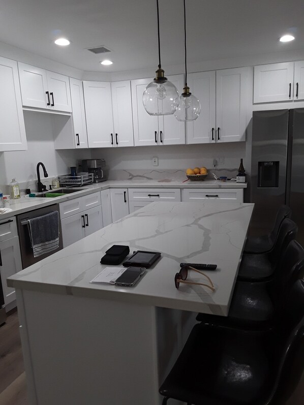 A modern kitchen with white cabinets, a marble countertop, and a built-in island with seating.