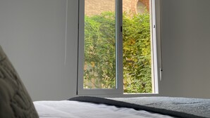 Ein Schlafzimmer mit großem Fenster, einem Bett und Blick auf ein Backsteingebäude sowie auf Grünflächen.