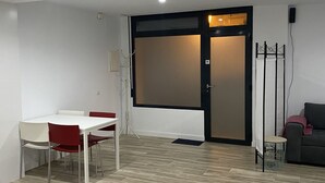 Ein Zimmer mit einem weißen Tisch und Stühlen, einem dunkelgrauen Sofa, einer Stehlampe und einer Tür zu einem anderen Raum.