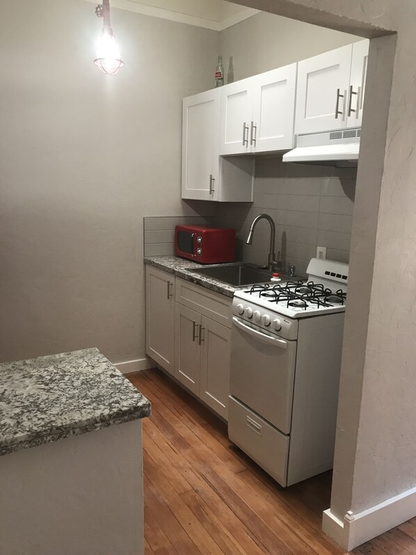 A compact kitchen with white cabinets, a red microwave, a gas stove, and a granite countertop. - Downtown Secluded & Peaceful Armory Park 10 min walk to Club Congress (Tucson)