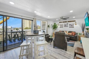 Un vaste espace de vie avec un balcon, un coin salon comprenant un canapé et des fauteuils, ainsi qu’un téléviseur fixé au mur.