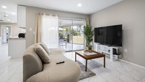 Ein modernes Wohnzimmer mit einer Couch, einem Couchtisch, einem Fernseher und einer Schiebetür zu einer Terrasse.