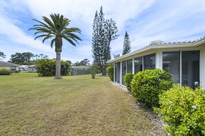 A residential property with a covered patio, a lawn, and mature trees.
