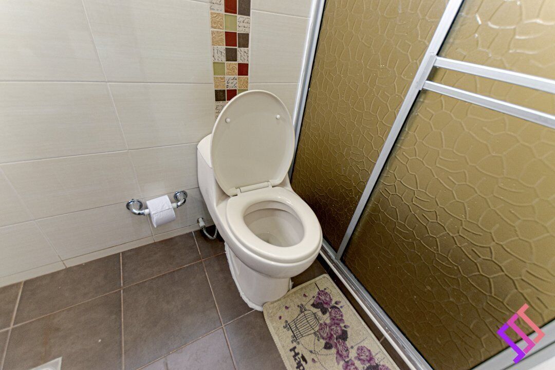 A bathroom with a toilet, a toilet paper holder, and a shower area with a textured wall.