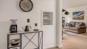 A modern living room with a coffee station, a round wall clock, and a bookshelf. - Beach St Escape-Hot tub-5min Walk to the Beach (Muskegon)