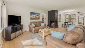 A modern living room with a flat-screen TV, a fireplace, and a dining area with a table and chairs. - Beach St Escape-Hot tub-5min Walk to the Beach (Muskegon)