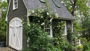 Ein kleines, eingeschossiges Gebäude mit Satteldach, einer weißen Garagentür und einem Fenster mit weißem Rahmen.