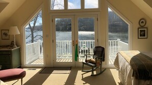 A room with a large bay window overlooking a lake, a rocking chair, and a bed.