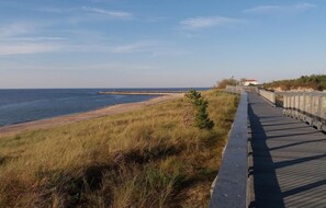 A wooden boardwalk along a beach with a clear view of the ocean and a distant pier.