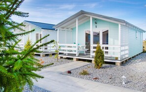 A two-story light blue cabin with a porch, numbered 5, featuring a picnic table and potted plants.