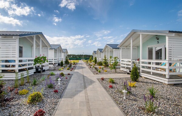 A row of white cabins with a gravel pathway leading to a grassy area.