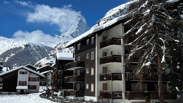 Une station de montagne enneigée, avec des bâtiments à plusieurs étages, des balcons et une clôture en bois.