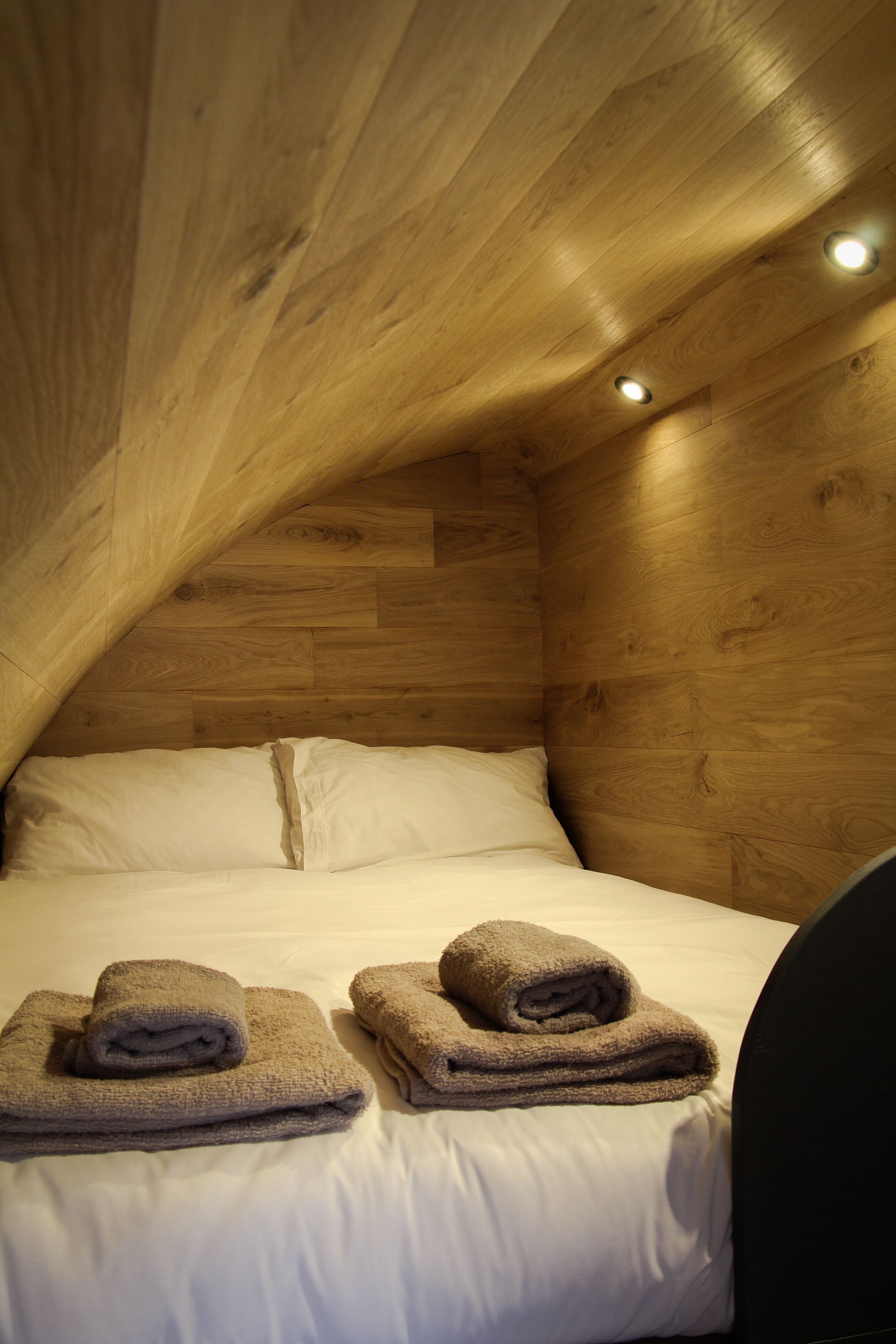 Un soffitto in legno con faretti, un letto con lenzuola bianche e due asciugamani piegati sul letto.