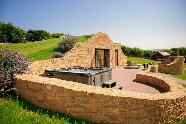 A stone hot tub with a patio area, surrounded by a stone wall, and a view of a grassy field.