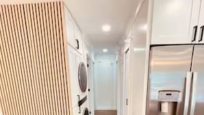 A modern kitchen with a stainless steel refrigerator, a built-in washing machine, and a wooden slatted cabinet.