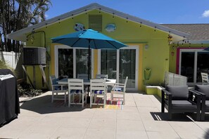 Une terrasse avec une table et des chaises, un climatiseur et un parasol bleu.