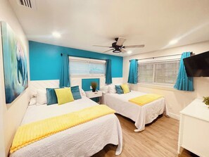 Une chambre d’hôtel avec deux lits, un ventilateur de plafond, une télévision et une fenêtre avec des rideaux.