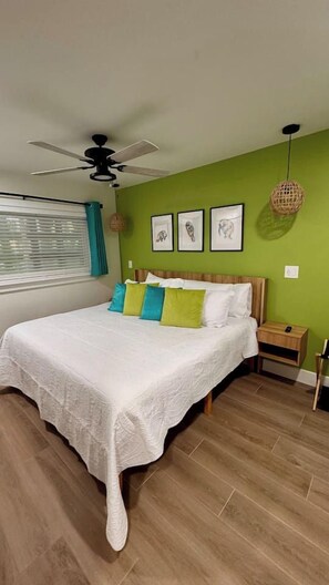 A bedroom with a bed, a ceiling fan, a bedside table, and a wall-mounted light fixture.