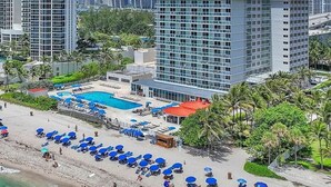 Un hôtel situé en bord de mer, doté d’une piscine, de parasols de plage et avec de grands immeubles en arrière-plan.
