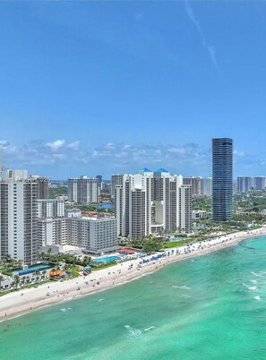 A coastal cityscape with high-rise buildings, a beach, and a clear blue sky. - Beachfront Studio with Balcony, Gym, Sauna & Parking at Marco Polo Beach Resort” (Sunny Isles Beach)