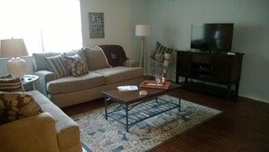 Ein Wohnzimmer mit einer Couch, einem Couchtisch, einer TV-Konsole und einem gemusterten Teppich.