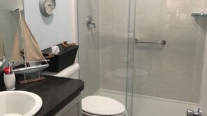 Ein Badezimmer mit Duschkabine aus Glas, einer weißen Toilette und einem Waschbecken mit dunkler Arbeitsplatte.