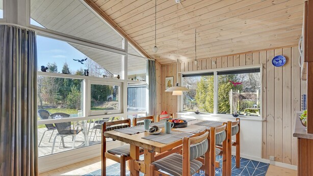 A wooden dining area with a table and chairs, large windows with curtains, and a view of the outdoors.