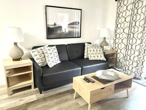 A living room with a black sofa, two side tables with lamps, a wooden coffee table, and a framed picture on the wall.