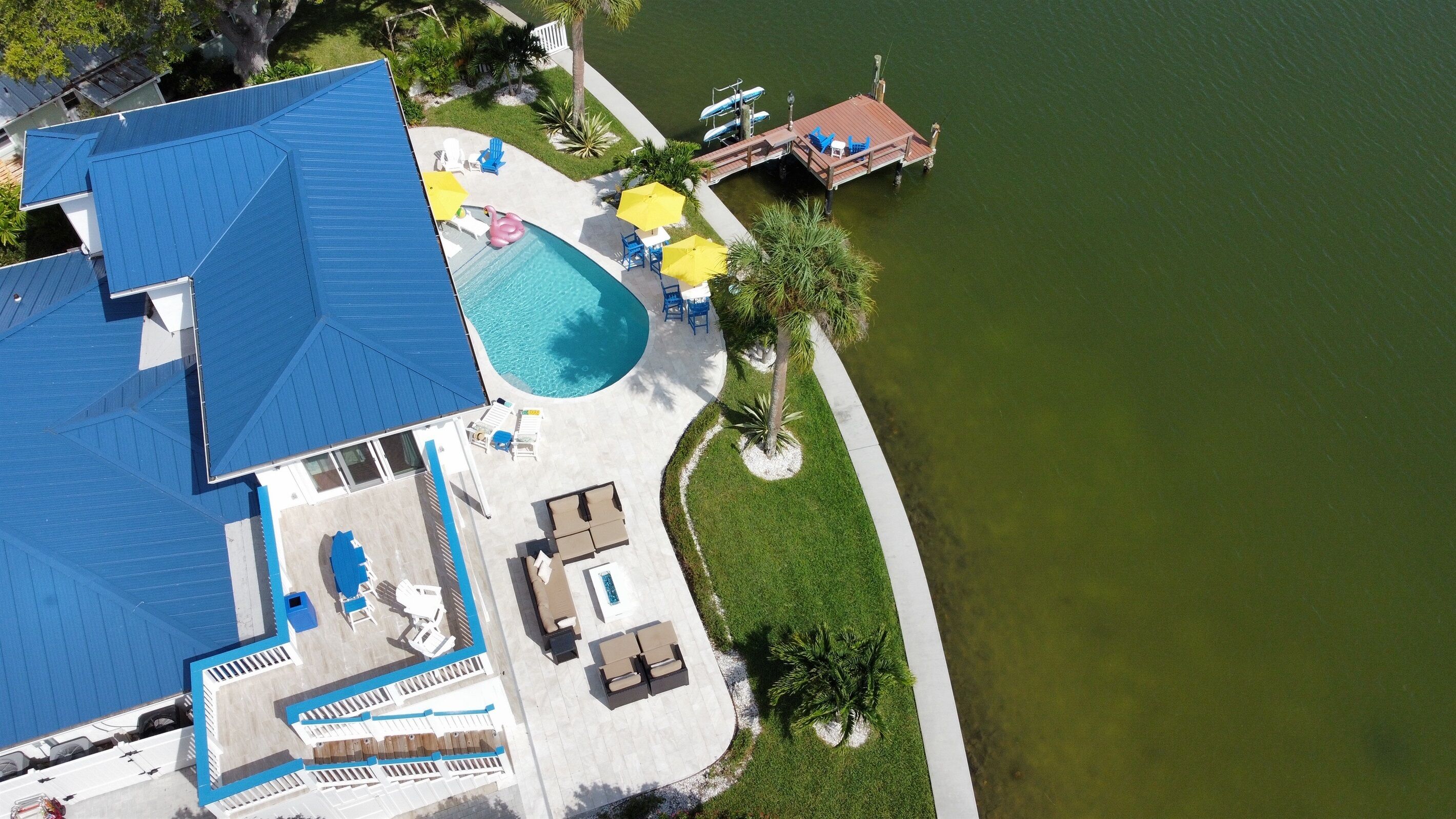Vista aérea de una propiedad con piscina, mobiliario exterior y muelle que se adentra en el agua.