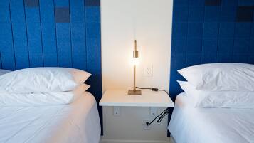 A hotel room with two beds, a nightstand with a lamp, and a wall with blue tiles.