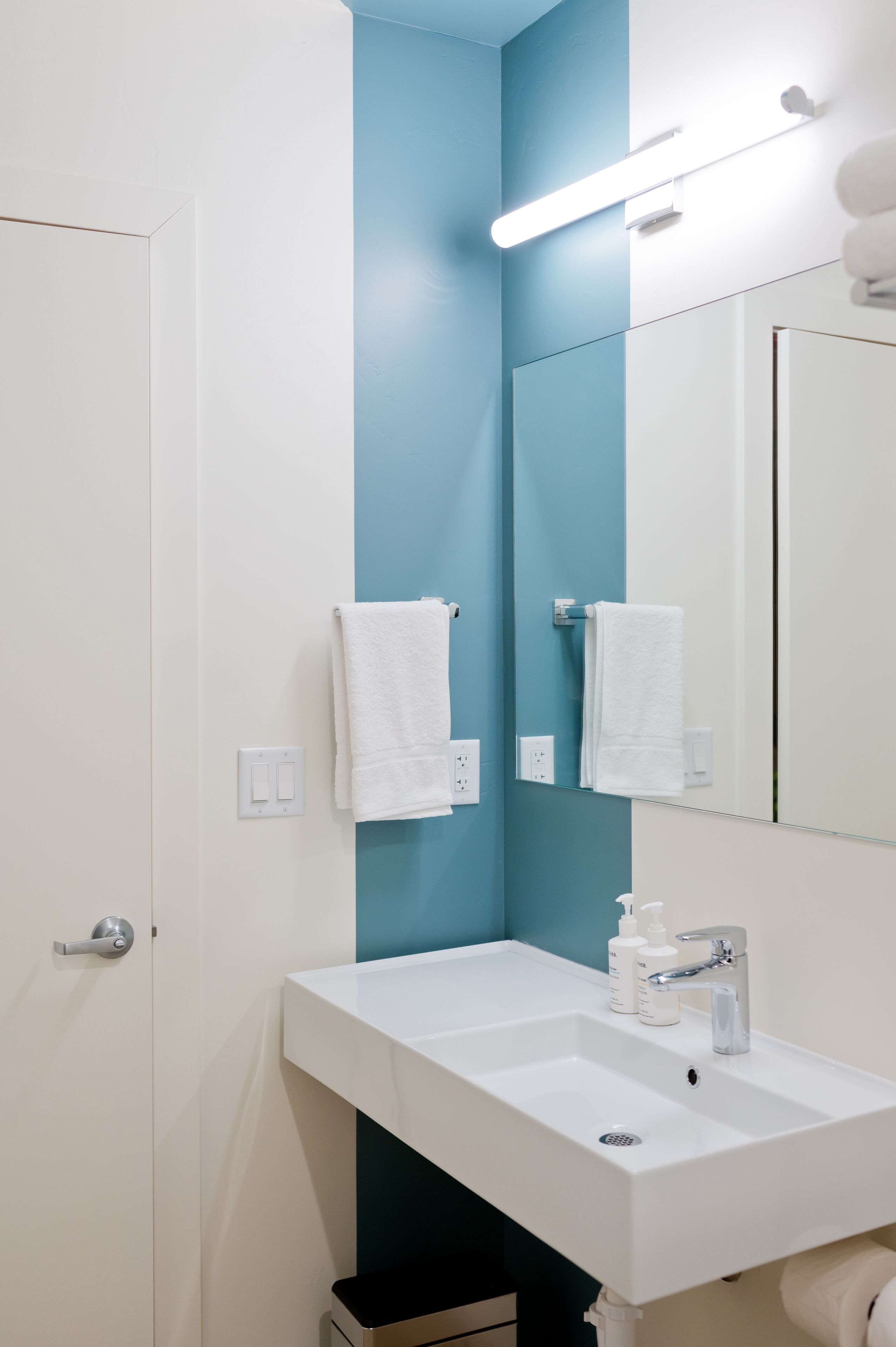 Une salle de bain avec un lavabo blanc, un mur d’accent bleu et un miroir au-dessus.