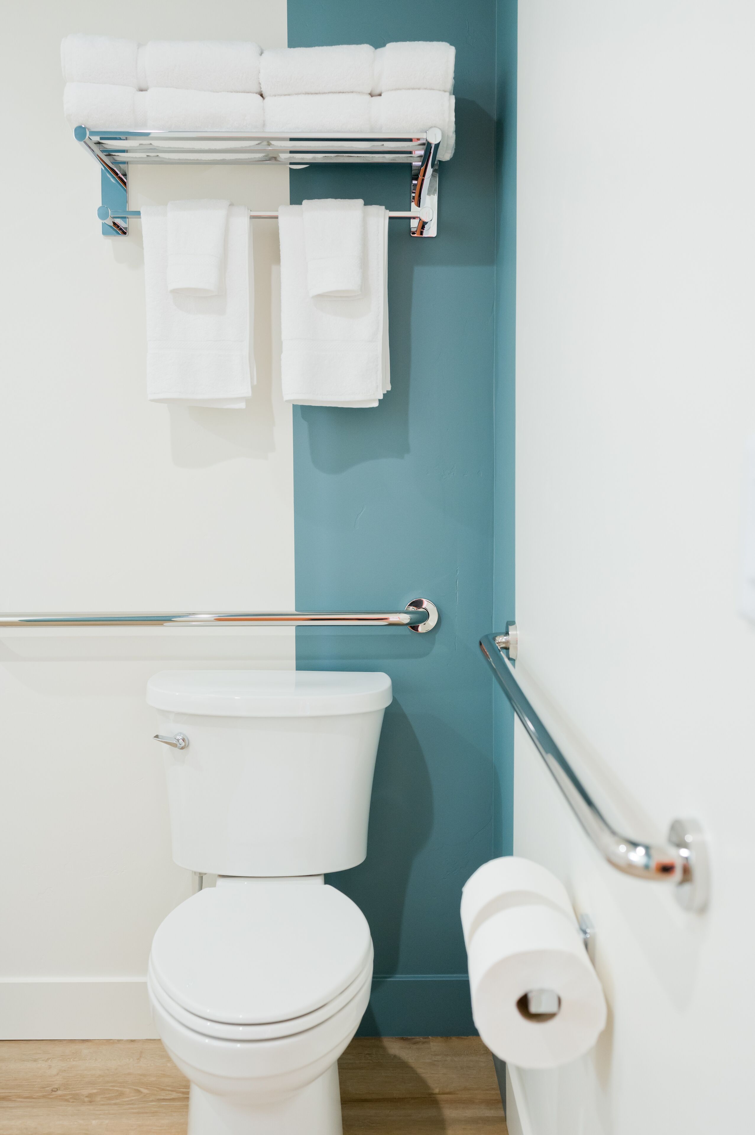 Un bagno con un WC bianco, una parete blu, un portasciugamani con asciugamani bianchi e una ringhiera.