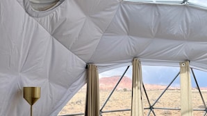 A geodesic dome tent with a floor lamp and curtains, set against a desert landscape. - Skyview Hotel (Torrey)